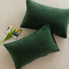 A dark green velvet throw pillow resting on a white surface with a small yellow flower and a card.