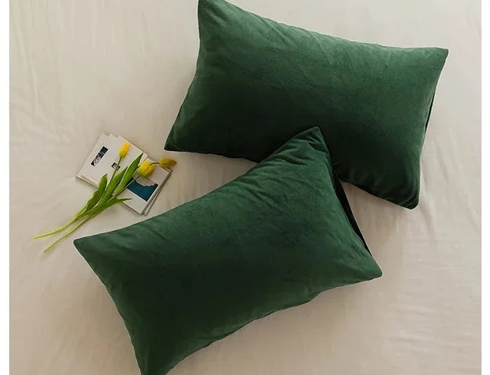 A dark green velvet throw pillow resting on a white surface with a small yellow flower and a card.