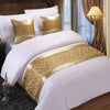 White bedding with gold patterned decorative bed flags on pillows and duvet.