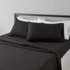 A set of four black microfiber flat fitted sheets on a bed with white pillows and bedding.