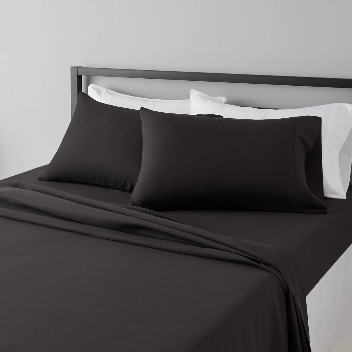 A set of four black microfiber flat fitted sheets on a bed with white pillows and bedding.