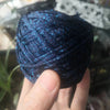 A hand holds a skein of dark blue glitter metallic yarn for crochet and knitting.
