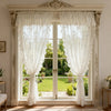 A pair of sheer white curtains with ruffled lace trim hang in a large window frame.