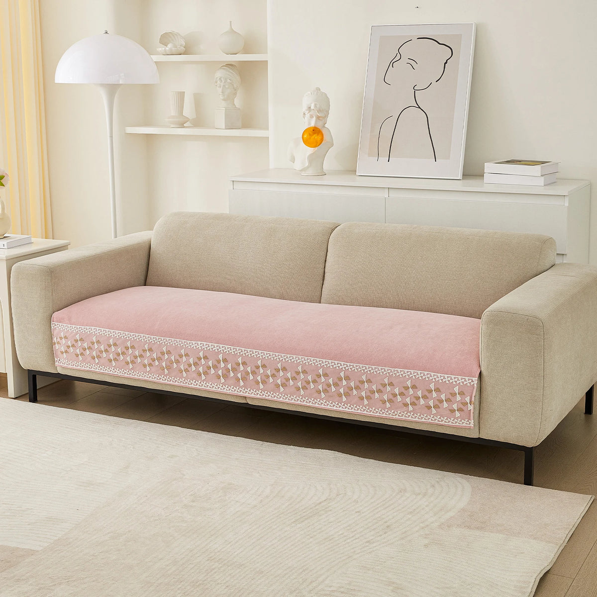 A beige sofa with a pink quilted cover featuring a lace trim, displayed in a bright living room setting.