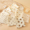 A collection of soft double-layer cotton baby swaddle blankets in cream and beige tones arranged on a light background.