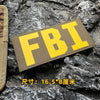 Yellow FBI patch with black stitching on a dark gray rock surface