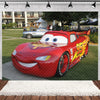A red cartoon race car model is displayed on a green lawn with a blurred background of buildings and trees.