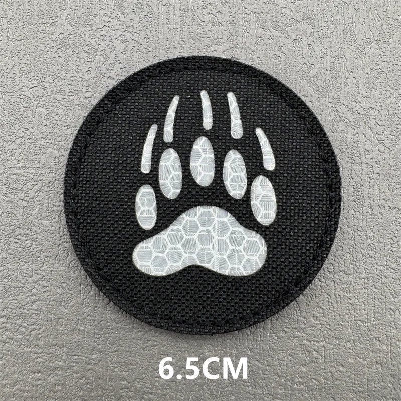 Black embroidered patch featuring a white paw print design on a gray background.