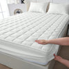 A white quilted waterproof mattress protector is shown on a bed, with a hand touching the fabric.