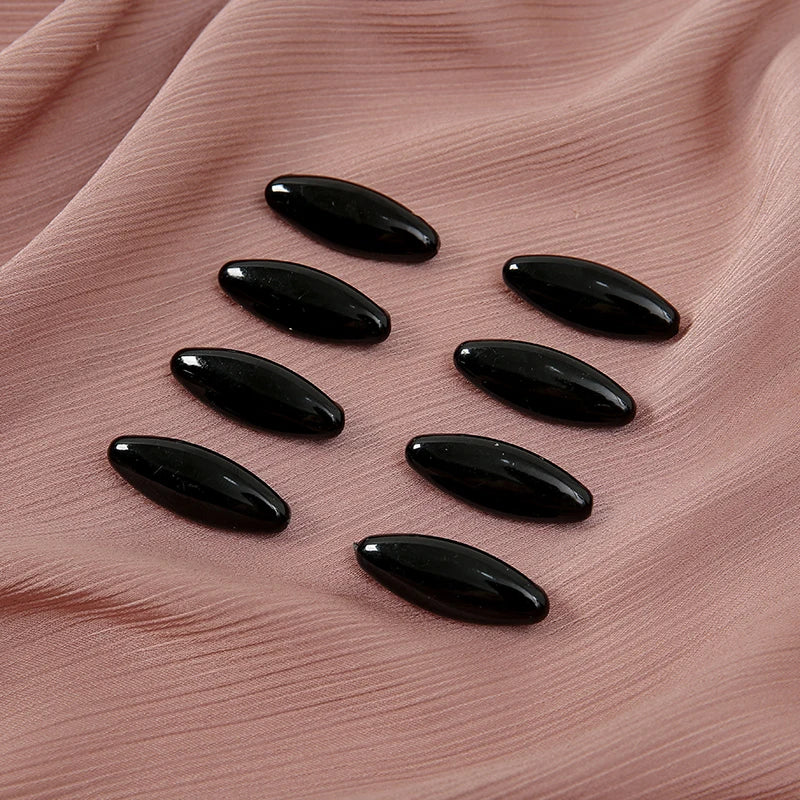 Eight black plastic safety pins arranged on a pink fabric background.