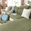 A plush olive green sofa cushion cover with striped fabric and white pillows on a light-colored sofa.
