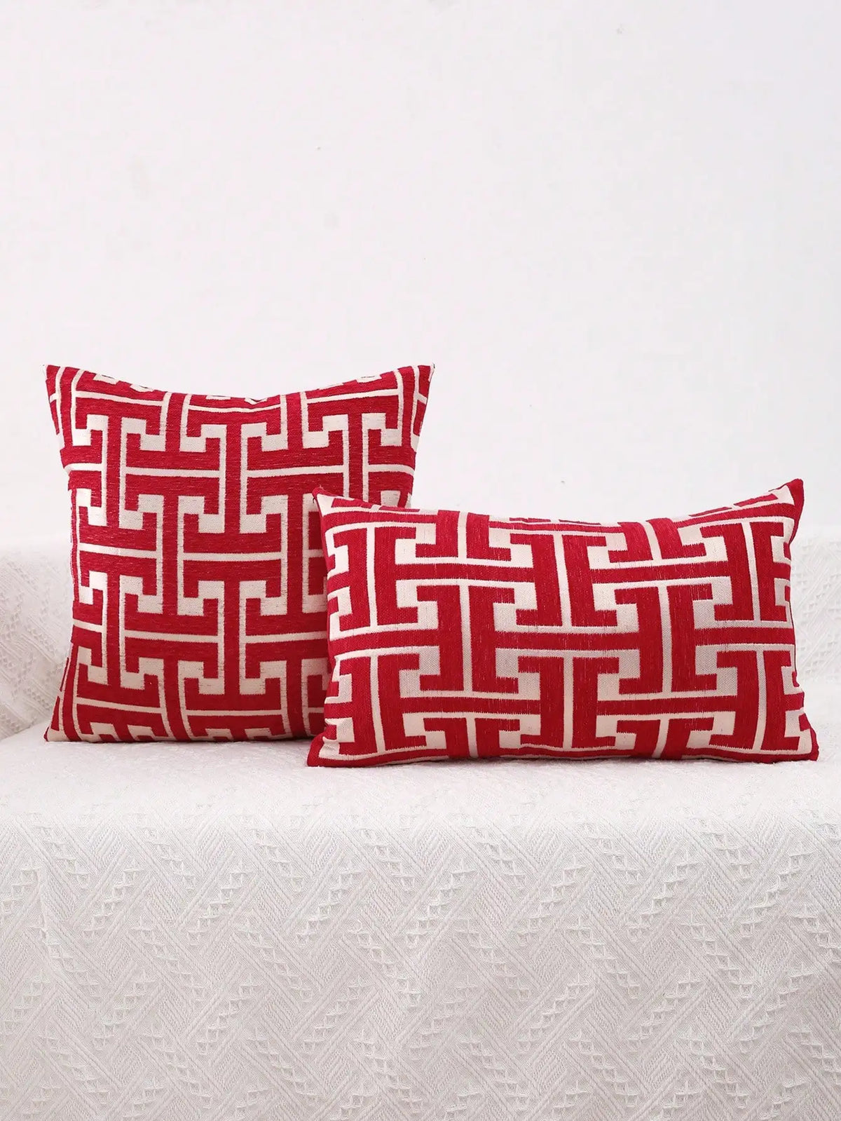 Two red and white geometric patterned throw pillows resting on a white textured surface.