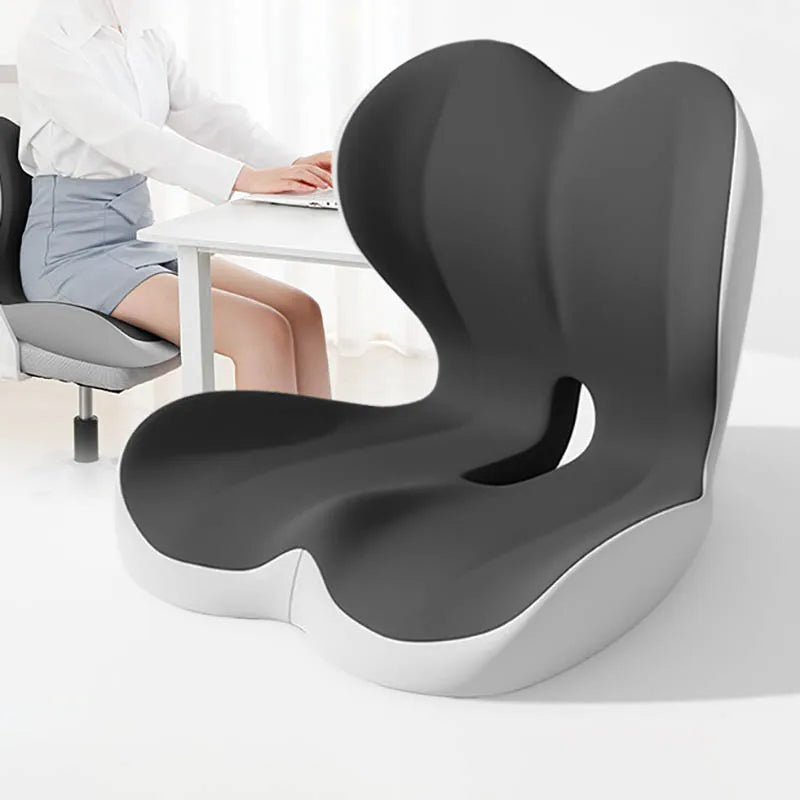 A gray ergonomic memory foam lumbar seat cushion is shown on a white desk with a person sitting nearby.