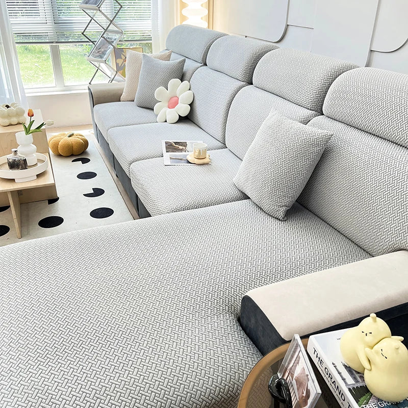 A light gray jacquard elastic sofa slipcover with white decorative pillows and a patterned floor.