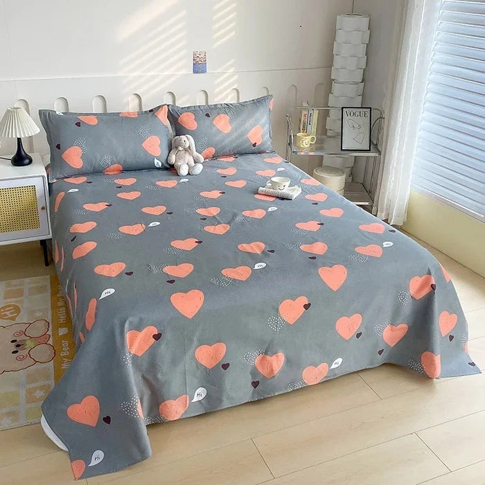 Gray flat bed sheets with a pattern of small orange hearts on a bed in a bright room.