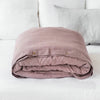 A folded mauve luxury French linen duvet cover resting on a white bed with white pillows.