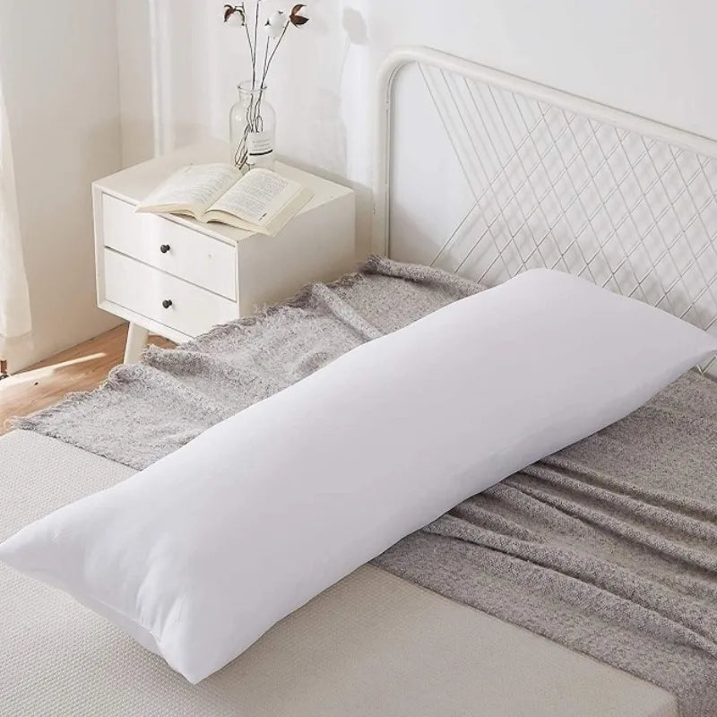 A white cushion on a bed with a light gray throw blanket and a white nightstand in a bright room.