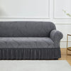 A charcoal gray jacquard stretch sofa cover featuring a leaf pattern displayed on a white floor.