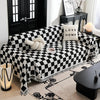 A black and white checkerboard sofa slipcover with a cream decorative pillow and a dark wooden cabinet in a living room.
