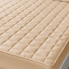 A beige quilted waterproof mattress protector with deep pockets shown on a bed.
