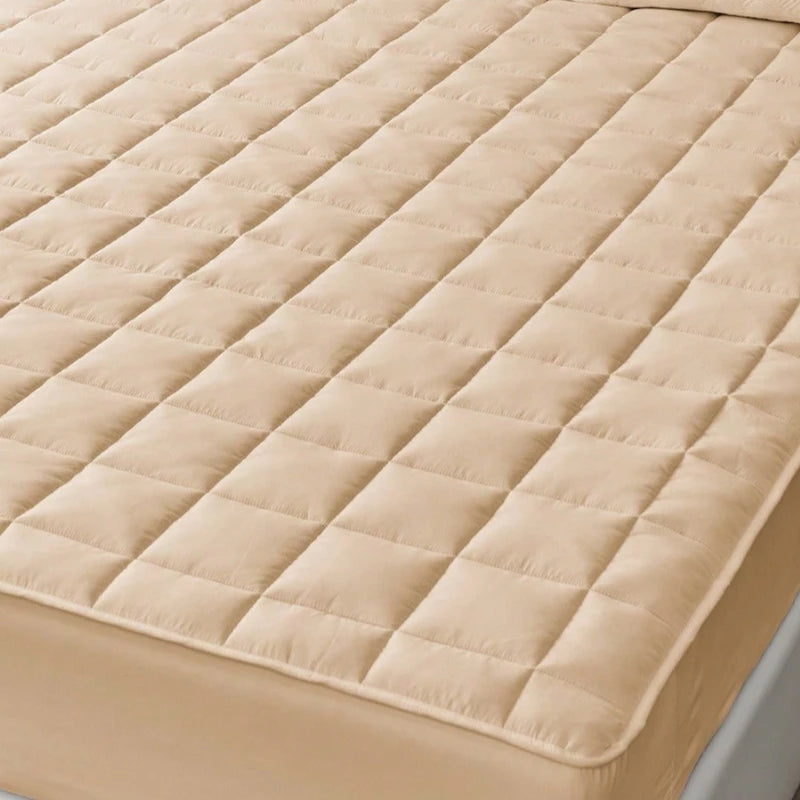 A beige quilted waterproof mattress protector with deep pockets shown on a bed.