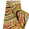A close-up of an African wax print fabric featuring a vibrant pattern of orange, yellow, and green leaves.