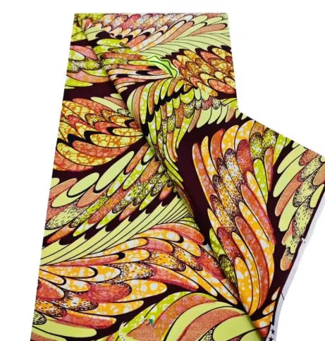 A close-up of an African wax print fabric featuring a vibrant pattern of orange, yellow, and green leaves.
