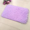A rectangular purple fluffy rug placed on a light wooden floor next to some pink flowers.