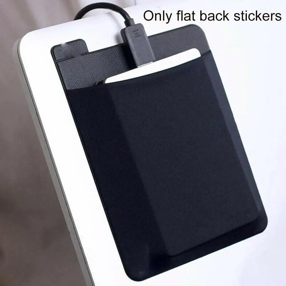 A black adhesive laptop back storage pouch with a flexible cord is shown against a white background.