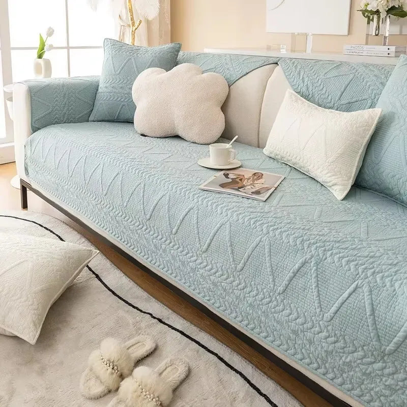 A light blue washed cotton sofa cover with a quilted texture and white accent pillows on a sofa.