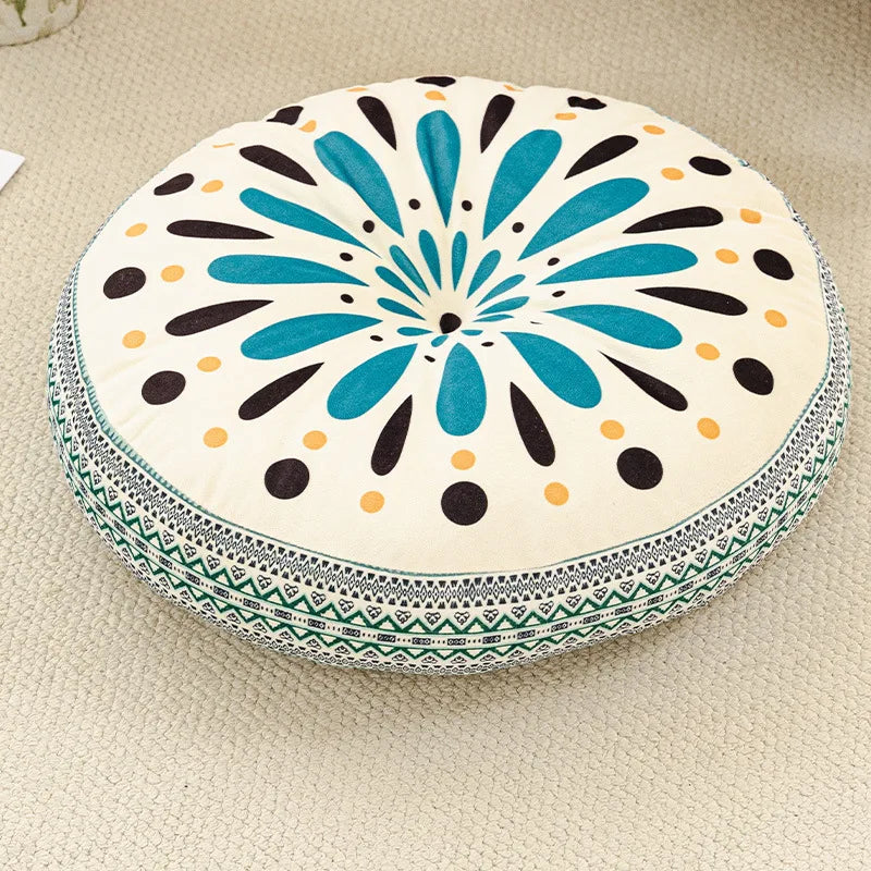 A round cushion with a bohemian pattern featuring teal, black, and cream dots and petals for floor seating.