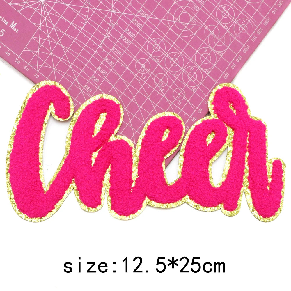 Pink felt cheer letter patch with gold glitter outline on a pink grid background