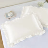 A set of two white ruffled satin pillowcases with silky envelope closures displayed on a white surface.