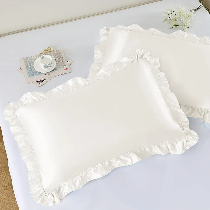A set of two white ruffled satin pillowcases with silky envelope closures displayed on a white surface.