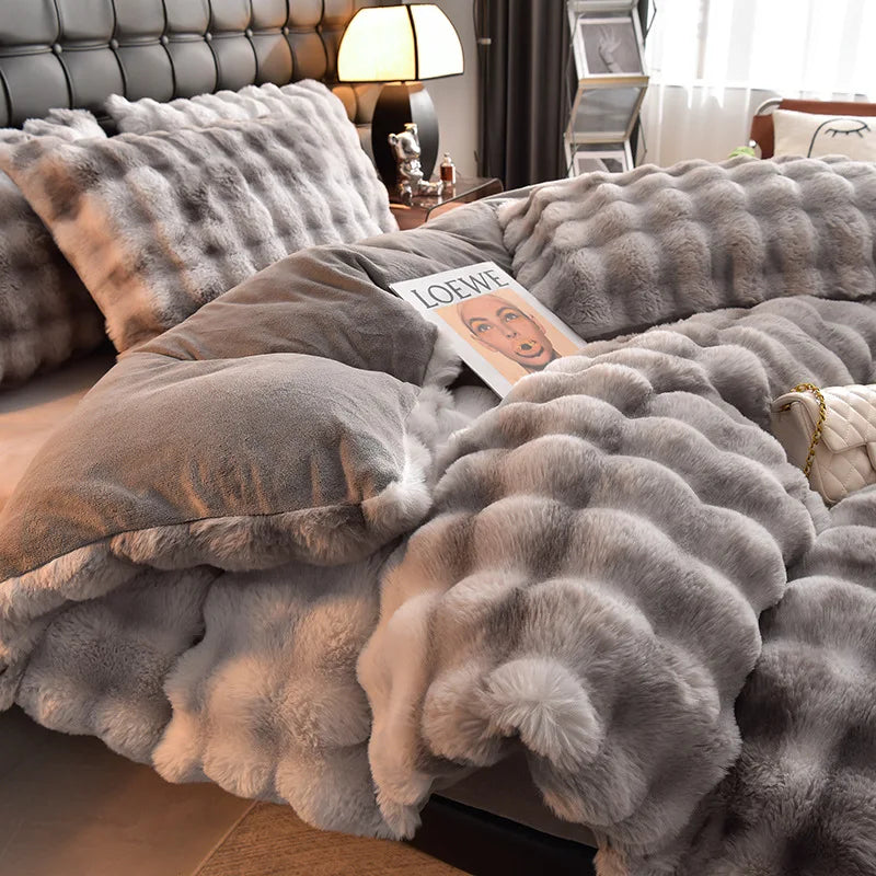A fluffy gray faux rabbit hair bedding set draped on a bed with dark curtains and a lamp.