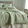 A light green luxury French linen duvet cover displayed on a bed with white linens and natural wood accents.