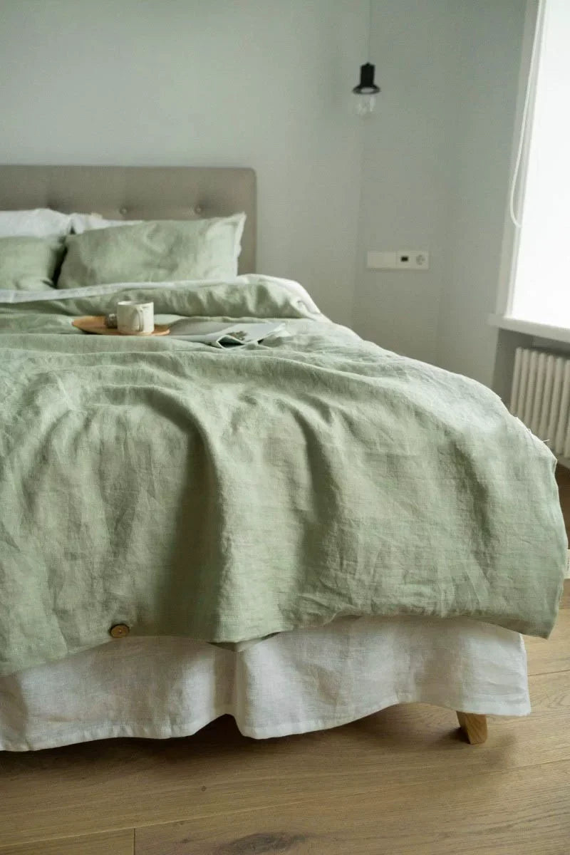A light green luxury French linen duvet cover displayed on a bed with white linens and natural wood accents.