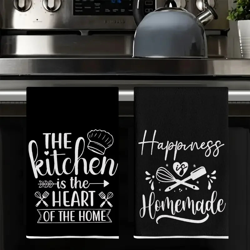 A set of two black absorbent kitchen cleaning towels featuring white text that reads The kitchen is the heart of the home and