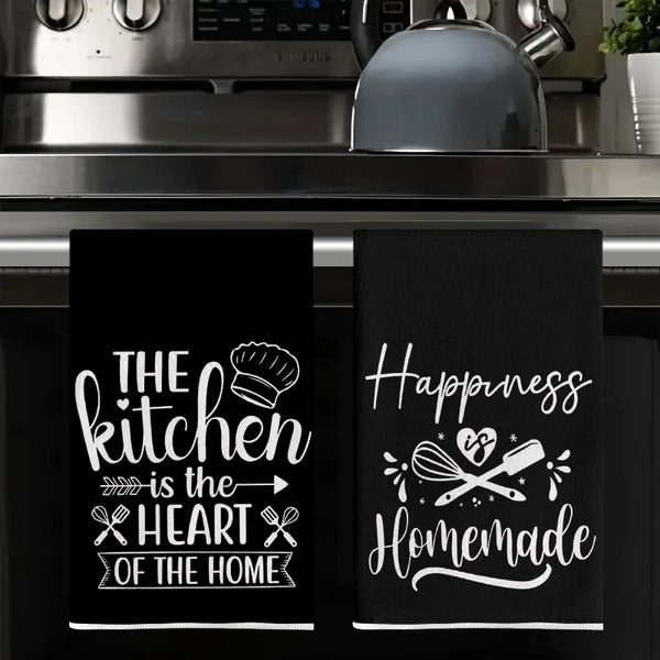 A set of two black absorbent kitchen cleaning towels featuring white text that reads The kitchen is the heart of the home and