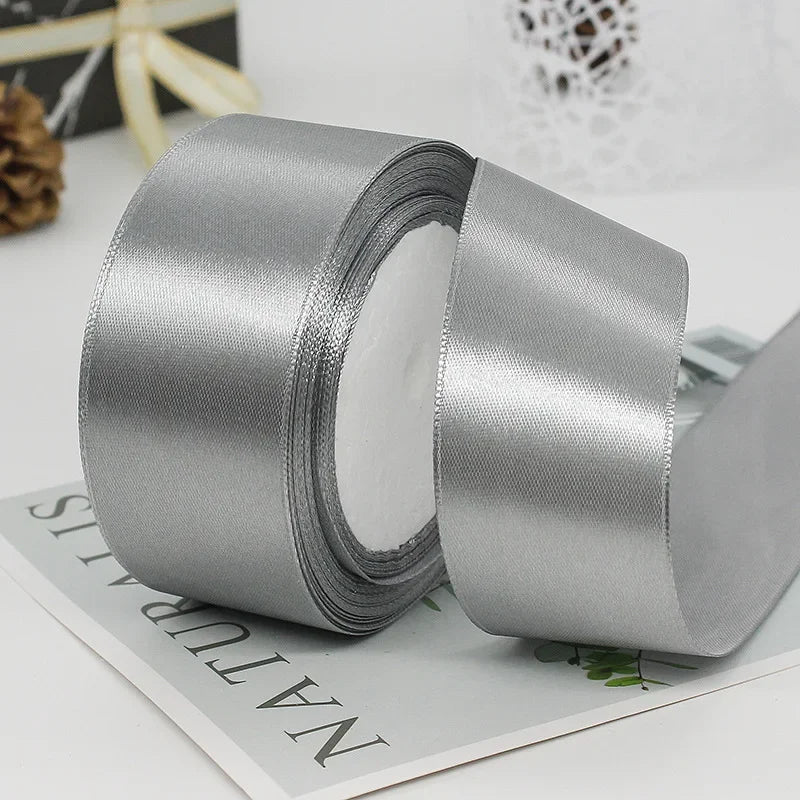 Rolls of silver satin craft ribbon shown on a white surface.