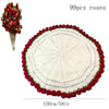 A round white knitted throw blanket with a red floral border and a decorative rose bouquet shown next to it.