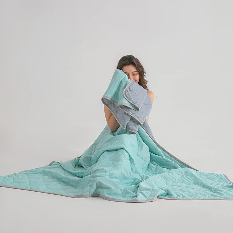 A person is using a light blue cooling blanket, draped over their head and body, against a plain background.