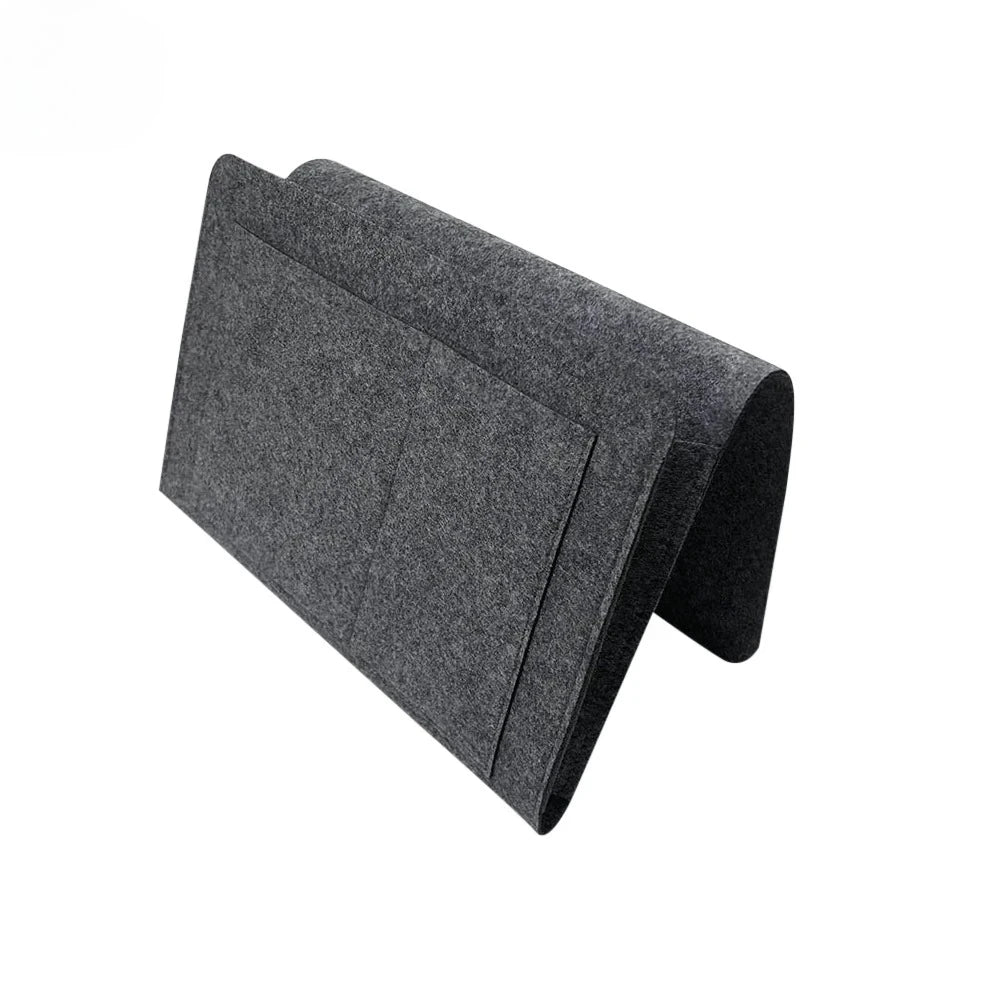 A dark gray felt bedside storage organizer with a hanging pocket.