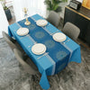 A long blue tablecloth set for dining or party decor with white plates and silverware on a gray table.
