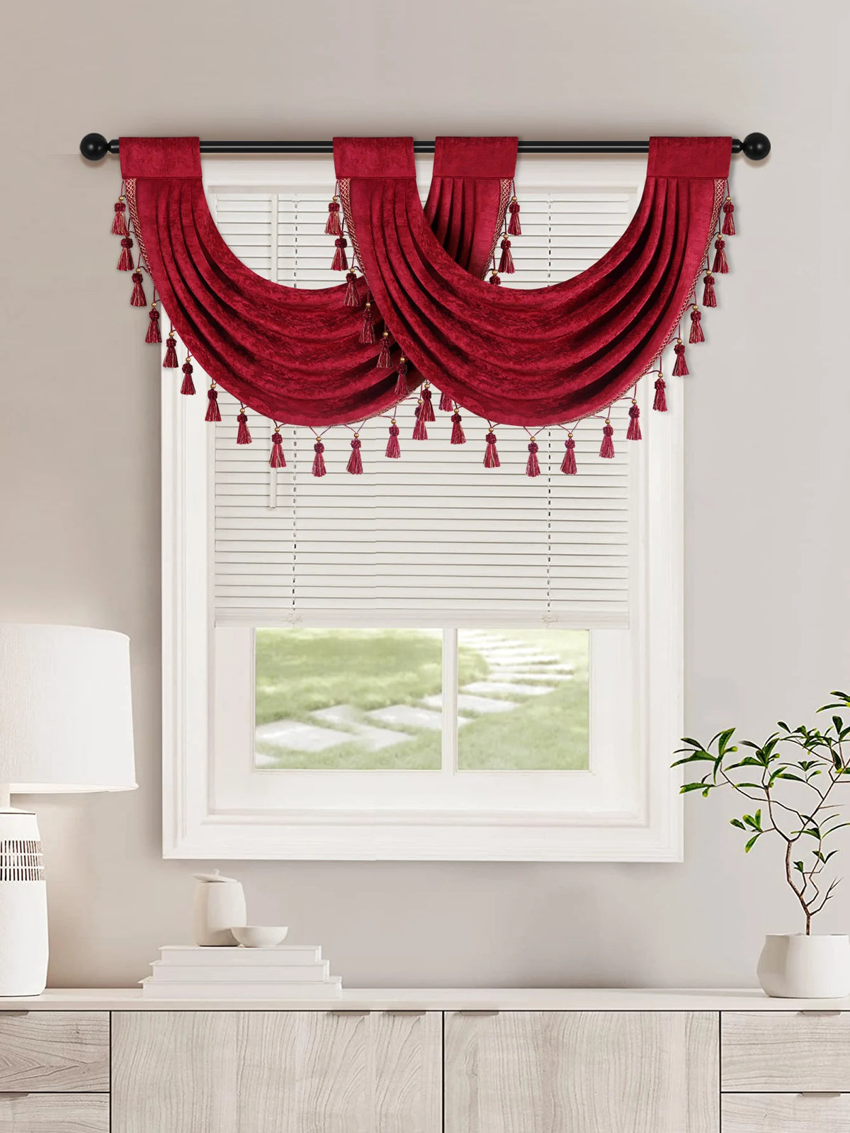 A deep red European style window curtain valance with tassels is displayed over a white plantation shutter window.