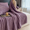 A purple faux fur throw blanket draped over a person on a bed, next to a candle and light curtains.