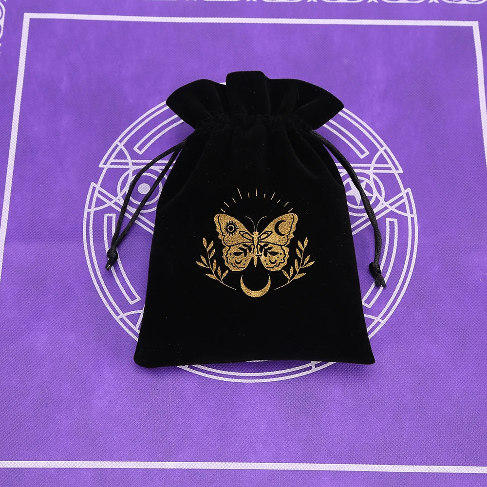 A black velvet pouch with gold foil butterfly and laurel design rests on a purple patterned surface.