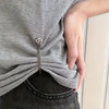 A close-up of a hand wearing a silver magnetic chain buckle on a gray t-shirt.
