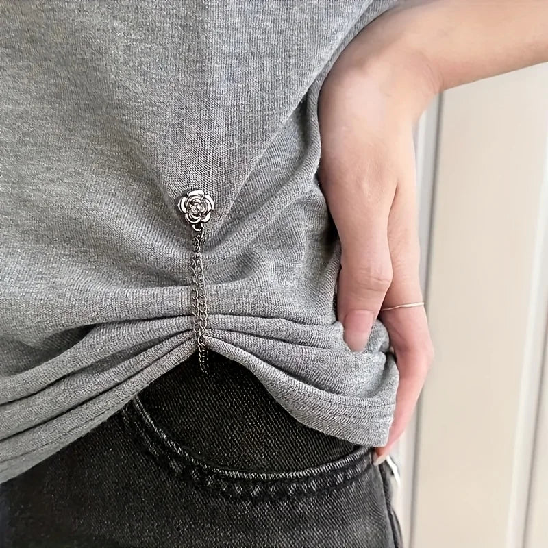 A close-up of a hand wearing a silver magnetic chain buckle on a gray t-shirt.
