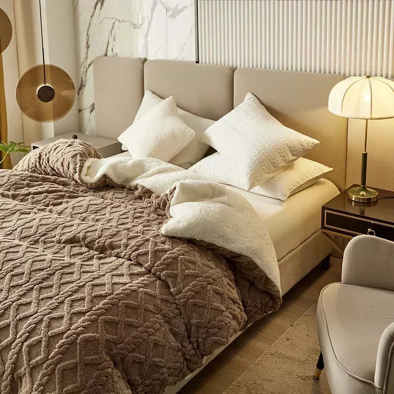 A cozy fleece blanket in beige and brown tones is draped over a bed with white pillows and modern lighting.